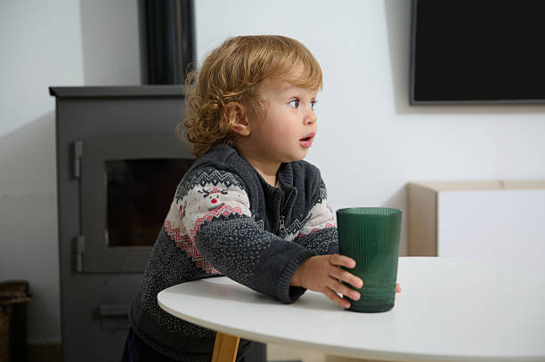 Child Sitting at Table Holding a Cup in Cozy Indoor Setting
