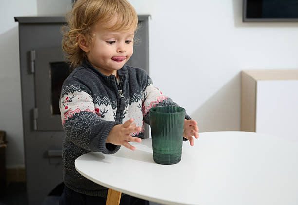 istock Young Child Playing With a Green Glass on a White Table Indoors 2205584220
