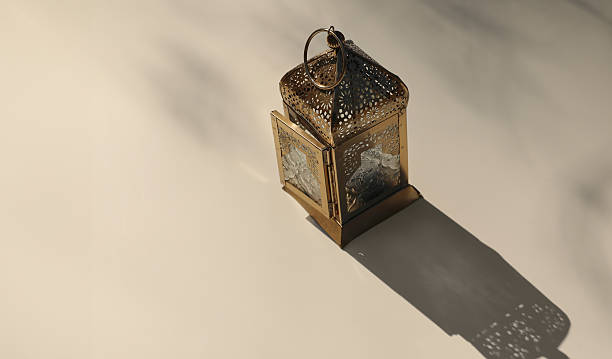 istock Golden metal ornamental Moroccan lantern on beige table in sunlight, long shadows. Blurred background, top view. Festive banner still life for Muslim holiday Ramadan Kareem. Eid mubarak celebration. 2205584603