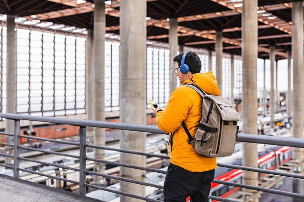 istock Young man with backpack and headphones using smartphone in train station 2205584877