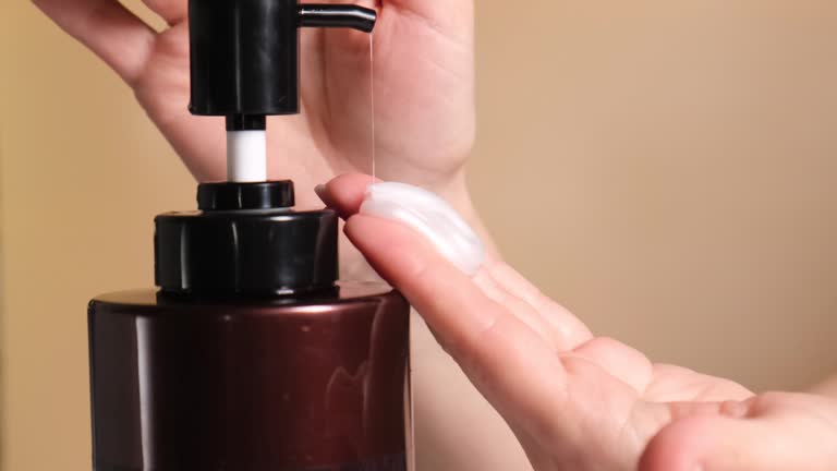 Female hands pressing a dispenser with cream, shampoo or conditioner, squeezing a face or body care product onto the hand, close-up shooting
