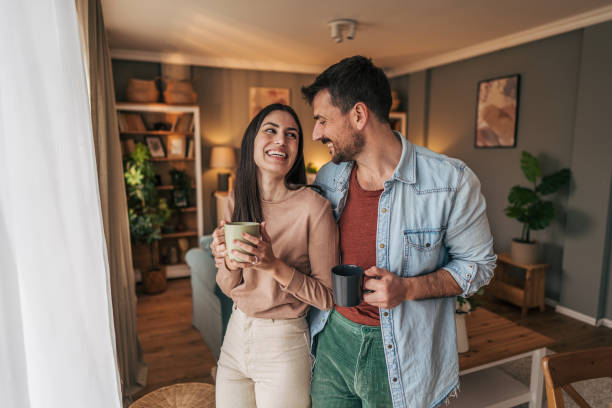 istock Young couple smiling and drinking coffee in living room 2205586570