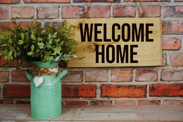 Welcome Home text on wooden sign hanging on old brick wall background