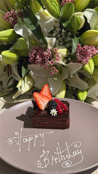 istock Elegant birthday chocolate cake garnished elegantly with fresh berries, cake placed artistically on beige plate near lush flower bouquet, ideal composition for celebrating intimate special occasions. 2205587786