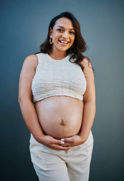 istock Smiling Pregnant Woman in White Against Blue Backdrop 2205589551