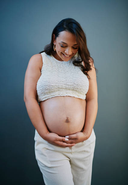 istock Smiling Pregnant Woman in White Against Blue Backdrop 2205589555