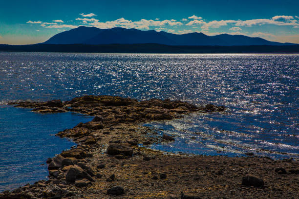Dramatic clouds fill the sky over Yellowstone Lake creating a striking contrast with the deep blue horizon. The rocky shoreline leads out toward a distant mountain range enhancing the distance of depth and natural beauty in Yellowstone National Park.