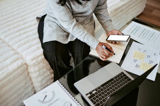 istock Focused Woman Writing Notes with Laptop and Smartphone 2205590183