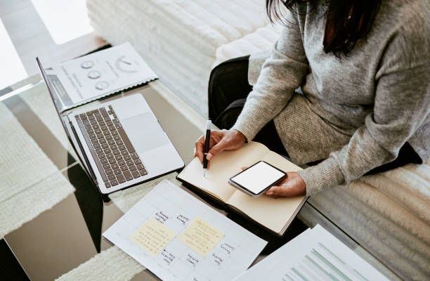 Focused Woman Writing Notes with Laptop and Smartphone