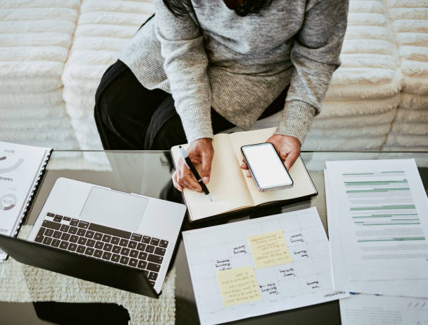 istock Focused Woman Writing Notes with Laptop and Smartphone 2205590203