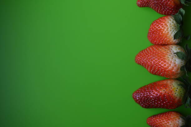 Fresh strawberries arranged on a bright green background, photographed in close-up. The image shows ripe fruit with visible texture and natural detail.