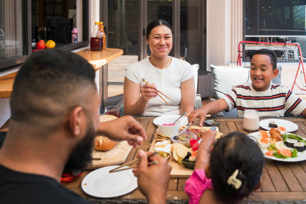 Maori family enjoying a healthy meal including fresh breads, fruits and other variety of food together at home gathered around dining table.
