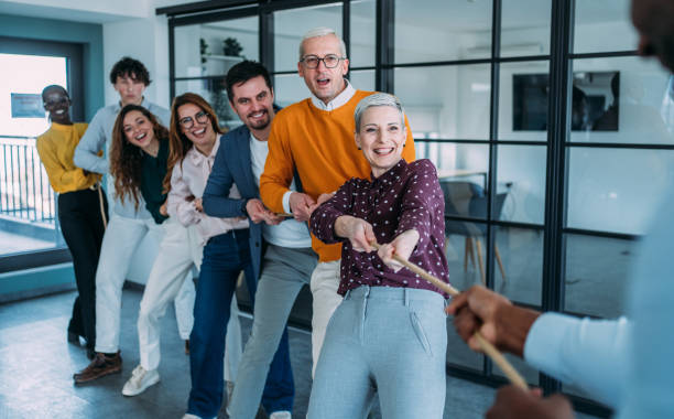 istock Playful colleagues having fun while playing tug-of-war in the office. 2205598329