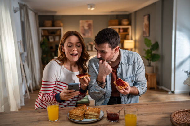 istock Happy couple enjoying waffles and orange juice while using smartphone at home 2205598651