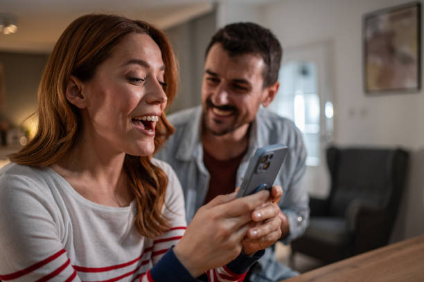 istock Happy couple sharing a funny moment while using a smartphone at home 2205598740