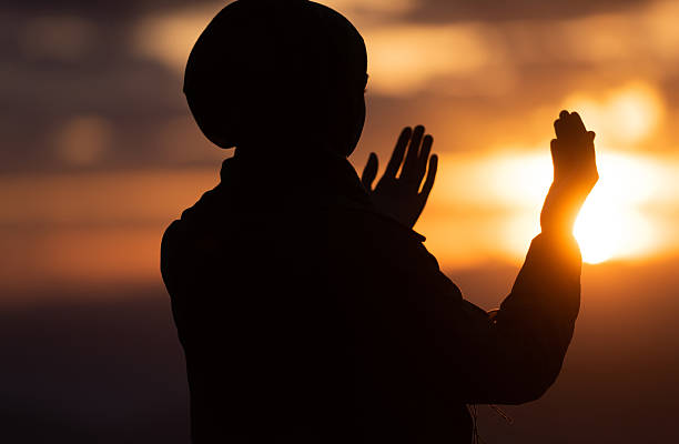 Silhouette of Muslim woman prayer having worship and praying with hands up at sunset. Silhouette of muslim woman prayer having worship and praying with hands open doing dua to Allah at sunset . High quality photo i love allah in arabic silhouettes stock pictures, royalty-free photos & images