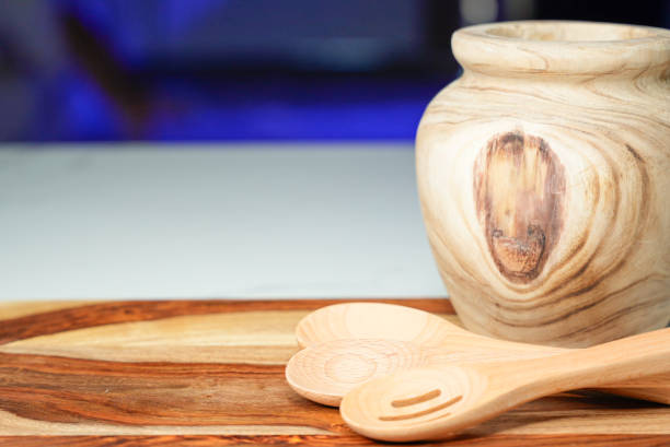 A rustic wooden jar with natural grain patterns and three wooden kitchen utensils placed on a polished wooden surface, creating a cozy and warm kitchen atmosphere.