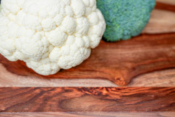 Close-up of fresh cauliflower and broccoli placed on a rustic wooden background. Ideal for healthy eating, organic food, and plant-based diet concepts.