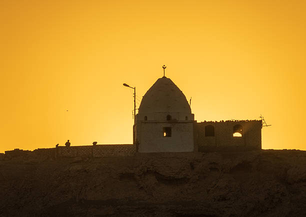 Single man stands by wall of a Mosque silhouetted against brilliant sunset sky along Nile River in Egypt