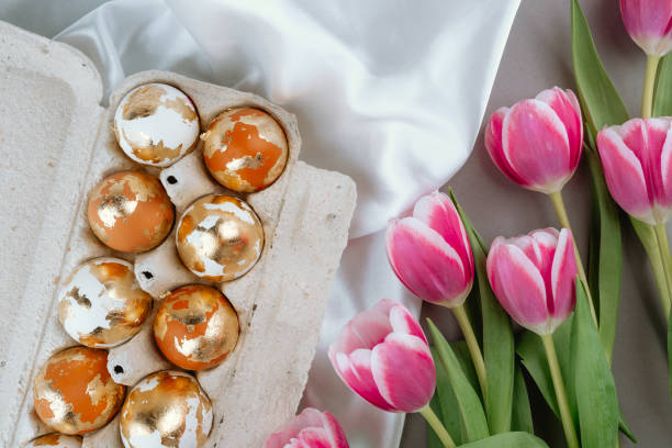 istock Gold Easter eggs in a carton box with pink tulips, top view. Easter festive background. 2205622726
