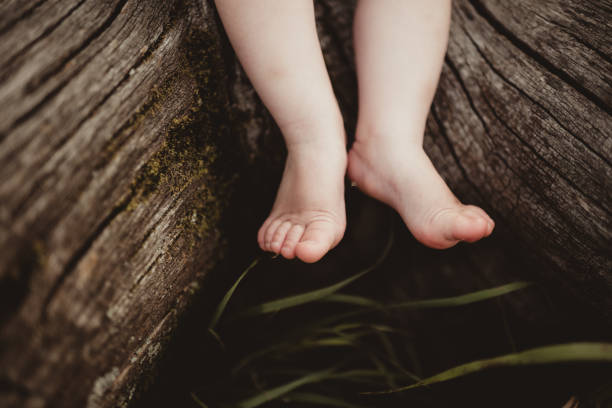 Child sitting barefoot climbing on wood log outdoors