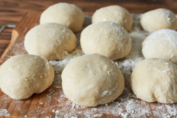 istock Raw dough balls with flour on wooden cutting board. Close up. 2205641908