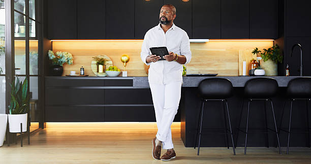 istock Kitchen, tablet and thinking with black man in home as real estate agent to search for interior design ideas. Future, planning and vision with serious mature person in apartment for property or real estate 2205648965