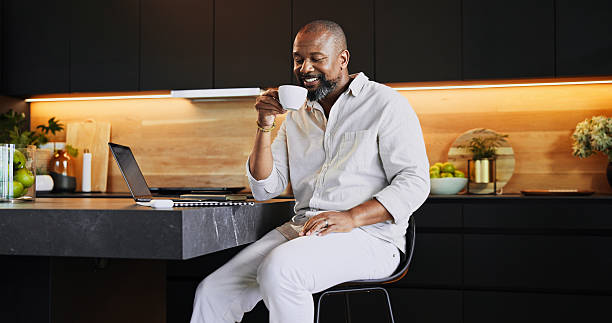 istock Remote work, coffee and black man in kitchen with laptop for research, online networking and website. Business entrepreneur, working from home and person with drink for break, wellness and relaxing 2205648992