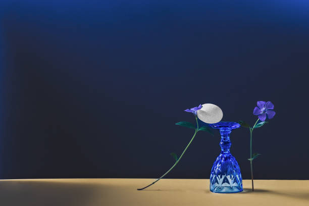 Abstract composition with periwinkle flowers, upside down blue wine glass and white stone.
