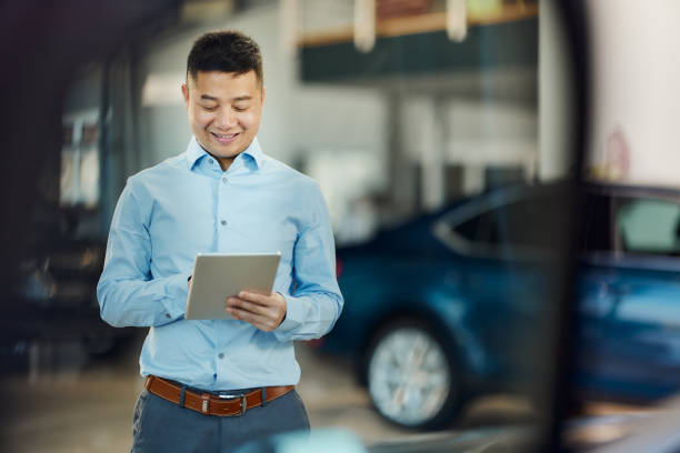 istock Happy Asian salesman using touchpad in a car showroom. 2205652420