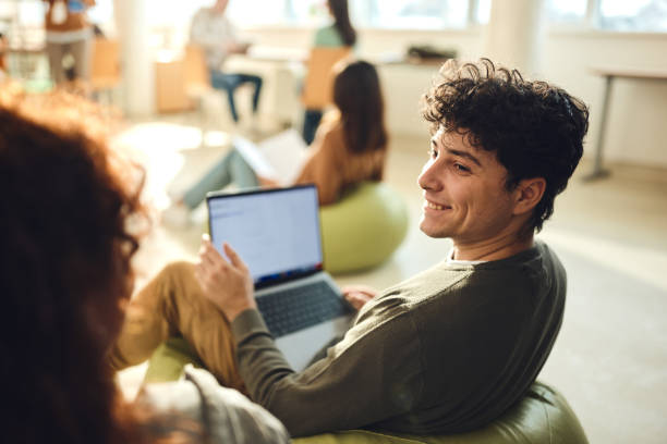 istock Happy male student talking to his friend while e-learning at casual classroom. 2205654839