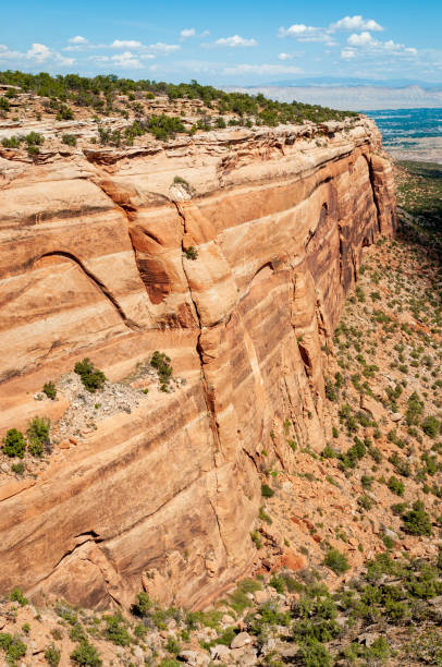A 1986 slide film image of Colorado National Monument, showcasing dramatic sandstone monoliths rising from the arid canyon floor. The towering spires and layered rock formations are etched with striations shaped by millennia of erosion, glowing in warm analog tones beneath a partly cloudy sky. The vintage film grain adds nostalgic depth to the rugged grandeur, evoking the spirit of mid-80s travel and the timeless power of the American Southwest.