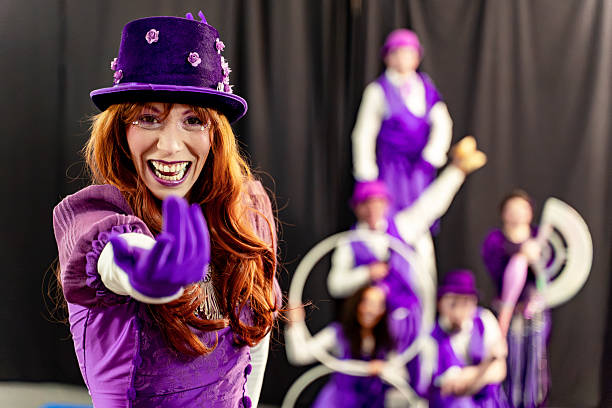 Redhead woman wearing a purple costume and hat, smiling and inviting the audience to the show