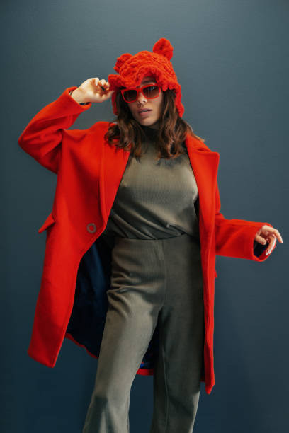 Fashion model wearing red woolen hat and sunglasses posing in studio with blue background