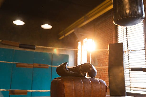 Boxing gloves lying down on boxing ring in empty gym. Equipment for fight training competition black protective boxing gloves ready for fighter winner on ring. Strength fit body workout training