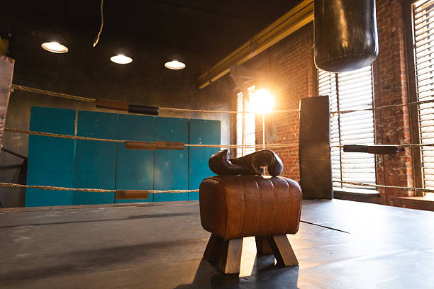 Boxing gloves lying down on boxing ring in empty gym. Equipment for fight training competition black protective boxing gloves ready for fighter winner on ring. Strength fit body workout training