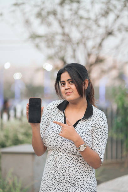 istock Confident Woman Presenting Smartphone with Blank Screen Outdoors 2205664949
