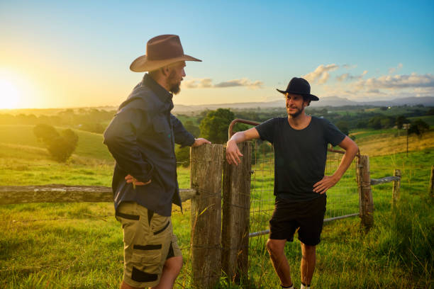 Two australian farmers discussing by fence at sunset Two australian farmers wearing hats discussing by a fence in a field at sunset farmer-drought-australia stock pictures, royalty-free photos & images