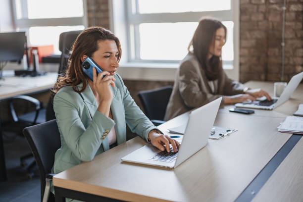 Woman on Phone While Working on Laptop in Office