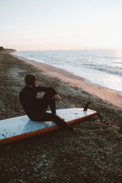 Photo of male surfer relaxing on the beach at sunset after an active day of surfing