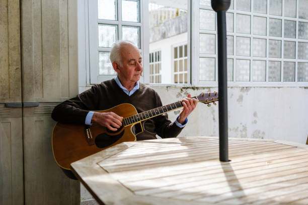 istock Senior man playing acoustic guitar at home by the window 2205678002