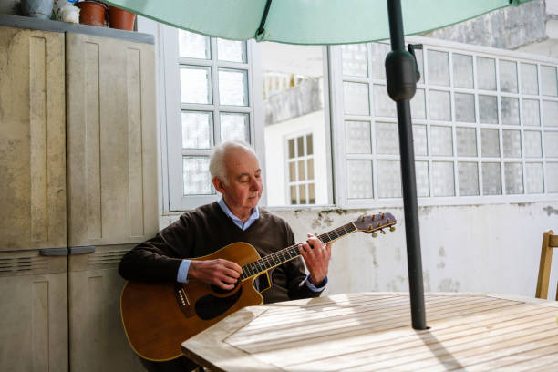 istock Senior man playing acoustic guitar at home by the window 2205678018