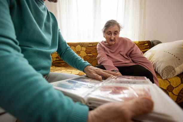 An elderly woman and her son sit together on the sofa, looking at vintage photos from their past.