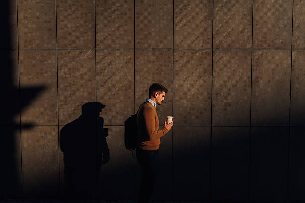 istock Businessman walking with coffee and backpack along modern building wall 2205686537