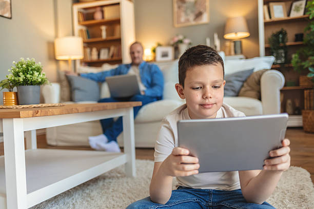 istock Cute boy using digital tablet while his father sitting on sofa, working on laptop at home. 2205688041