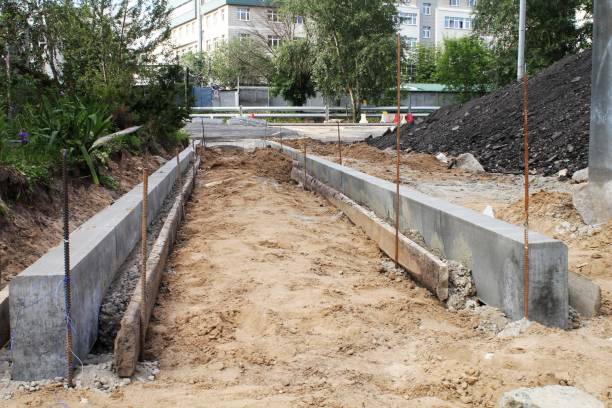 istock Concrete curbing installation at construction site. Pre-cast curbs in prepared bed. Concrete edging at construction zone. Concrete curbs laid in sandy terrain. Construction site with concrete kerbing 2205688044