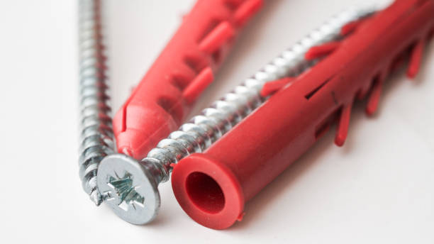 A close-up of silver Phillips head screws paired with red wall plugs, essential tools for secure mounting on walls and surfaces.
