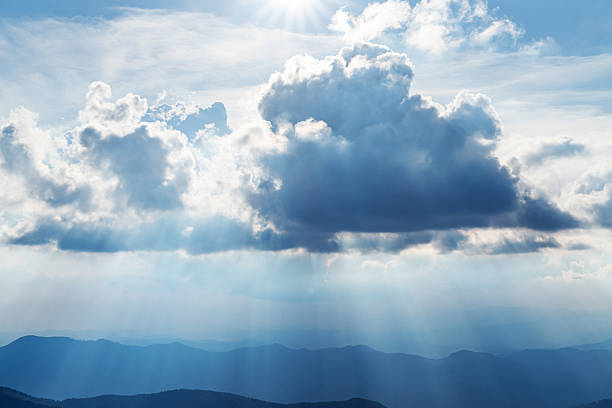 Morning sun rays highlighting misty blue mountains in spring. Serene and majestic nature photography
