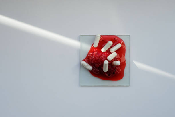 Vibrant red berry juice, and white capsules on white surface. Health, biologically active supplements. Sunbeam. Copy space.