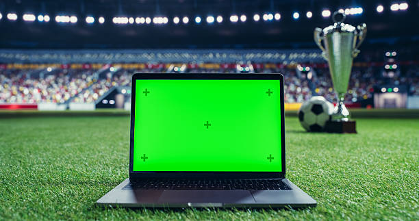 istock Laptop Computer with a Green Screen Template Standing on a Soccer Pitch with a Trophy and Soccer Ball in the Background. Mock Up Display Suitable for Adding Sports Themed Digital Content 2205704900